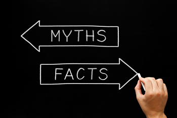 A person writing myths and facts with white chalk on a blackboard