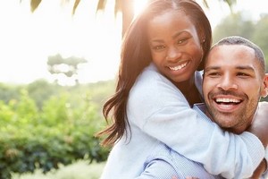 A man and woman smile and hug joyfully in the sunlight, celebrating their FHA 203b loan program success.  