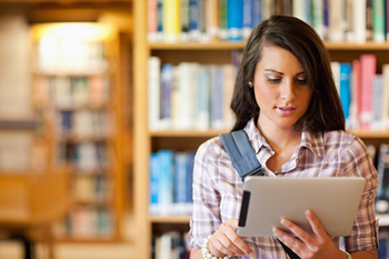 A young woman researching FHA financing articles on a tablet in a library.