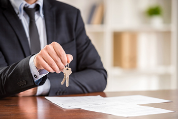 A man in a suit proudly holds a house key, symbolizing new beginnings and homeownership.  